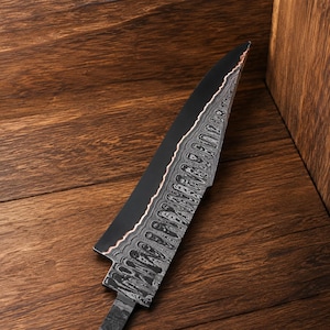 May include: A kitchen knife blade featuring a matte black finish on the upper portion and a complex, wavy silver and dark gray Damascus steel pattern on the lower edge, separated by a thin copper-colored line along the spine of the blade.