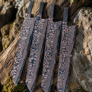 May include: Four knife blades featuring a distinct copper and dark steel pattern with a layered, wavy aesthetic. Each blade has a rectangular tang extending from the top, showcasing a complex, high-contrast metal texture across the entire surface.