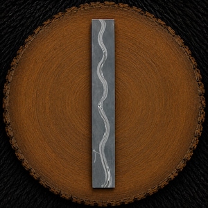 Pode incluir: Uma barra metálica retangular com acabamento cinza escuro e um padrão de linha vertical ondulada de cor clara que percorre o centro. A superfície apresenta uma textura mate e lisa com um elemento de design orgânico e fluido.