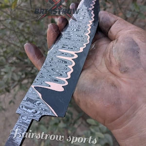May include: A Damascus steel knife blade with a dark finish and a wavy pattern. The blade has a decorative edge and a copper-coloured accent. The text "Bairstrow sports" is visible on the blade.