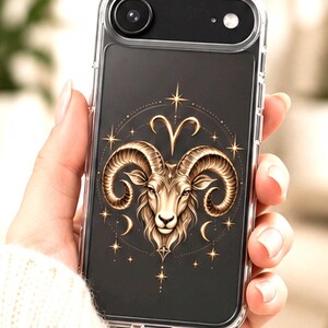 Puede incluir: Una funda transparente para smartphone con una ilustración en tono dorado de una cabeza de carnero Aries centrada en un marco circular. El diseño incluye pequeñas estrellas doradas, lunas crecientes y el símbolo del zodiaco Aries.