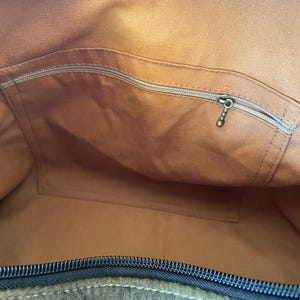 Pu&ograve; includere: Vista interna di una borsa tote in pelle marrone. La borsa ha un ampio scomparto principale, una tasca con cerniera e una tasca aperta pi&ugrave; piccola. La cerniera &egrave; nera e la fodera &egrave; di una tonalit&agrave; di marrone pi&ugrave; chiara.