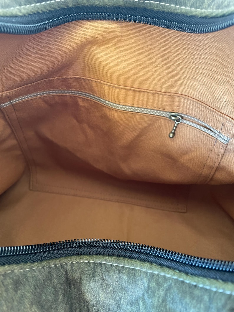 Pu&ograve; includere: Vista interna di una borsa tote in pelle marrone. La borsa ha un ampio scomparto principale, una tasca con cerniera e una tasca aperta pi&ugrave; piccola. La cerniera &egrave; nera e la fodera &egrave; di una tonalit&agrave; di marrone pi&ugrave; chiara.