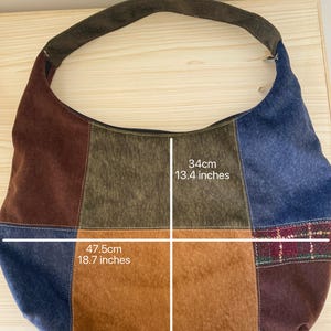 Pu&ograve; includere: Borsa a tracolla patchwork con manico in pelle scamosciata marrone. La borsa &egrave; realizzata con vari tessuti nei toni del marrone, blu e beige. La borsa &egrave; lunga 47,5 cm e larga 34 cm.