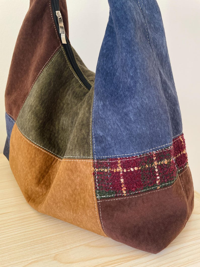 Pu&ograve; includere: Borsa a tracolla patchwork nei toni del marrone, blu e verde oliva. La borsa &egrave; dotata di chiusura con cerniera e di una sezione in tessuto scozzese rosso e verde. La borsa &egrave; realizzata in un materiale morbido simile alla pelle scamosciata.