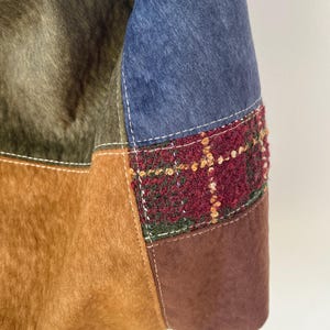 Pu&ograve; includere: Primo piano di una borsa patchwork con varie trame e colori. La borsa incorpora sezioni di tessuti marroni, verde oliva e blu, con un accento tartan strutturato in bordeaux, verde e oro. Le cuciture bianche delineano le cuciture.