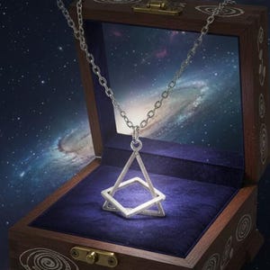 May include: A silver pendant necklace with a geometric design, presented in a wooden jewellery box with a blue velvet interior. The box is open, with a galaxy backdrop.