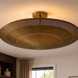 May include: A circular flush mount ceiling light fitting with an antique brass finish. The wide, shallow, bowl-shaped shade features two concentric rings of small, perforated holes that allow light to pass through, creating a glowing effect.