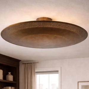 May include: A bronze-colored, circular flush mount ceiling light fixture. The fixture has a perforated border and a slightly domed center. The light is mounted on a white ceiling, and the room has a dark wood cabinet and a window.