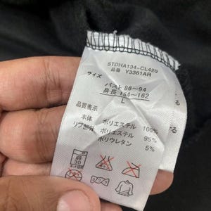 Puede incluir: Primer plano de una etiqueta de ropa con texto en japon&eacute;s. La etiqueta incluye detalles sobre la talla, la composici&oacute;n del material (poli&eacute;ster y poliuretano) y las instrucciones de cuidado. La etiqueta es blanca con texto negro.