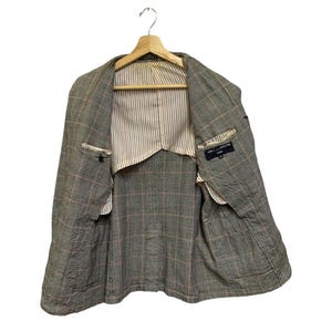 Op de afbeelding: Een grijze blazer met een ruitpatroon, hangend aan een houten hanger. De blazer heeft een gestreepte voering en zichtbare zakken. Het open ontwerp onthult de binnenconstructie en het label.