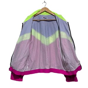 May include: A vintage FILA jacket, open to display the interior lining. The jacket features a neon green hood and a color-blocked design in blue, yellow, and pink. The FILA logo is visible on the chest.