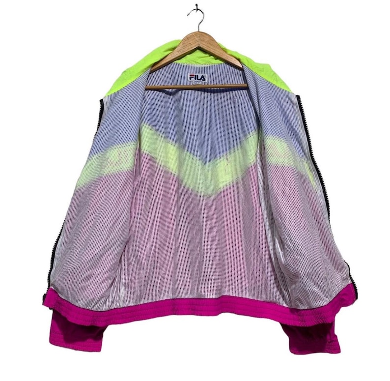 May include: A vintage FILA jacket, open to display the interior lining. The jacket features a neon green hood and a color-blocked design in blue, yellow, and pink. The FILA logo is visible on the chest.