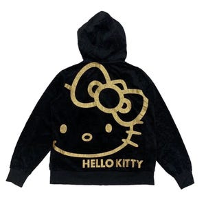 Puede incluir: Sudadera con capucha negra con un dise&ntilde;o de Hello Kitty dorado con purpurina en la espalda. El dise&ntilde;o incluye la cara del personaje y las palabras "Hello Kitty" debajo. La sudadera tiene una cremallera completa y una textura suave y aterciopelada.