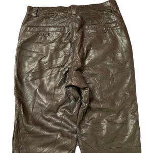 May include: Brown leather pants with a classic design. The pants feature two back pockets with button closures and a belt loop waistband. The leather has a slightly wrinkled texture, giving the pants a vintage look.