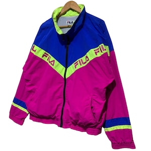 May include: A vintage Fila track jacket in a vibrant color block design. The jacket features a combination of blue, pink, and neon green. The Fila logo is prominently displayed across the chest and sleeves. It has a full zip closure and a stand-up collar.
