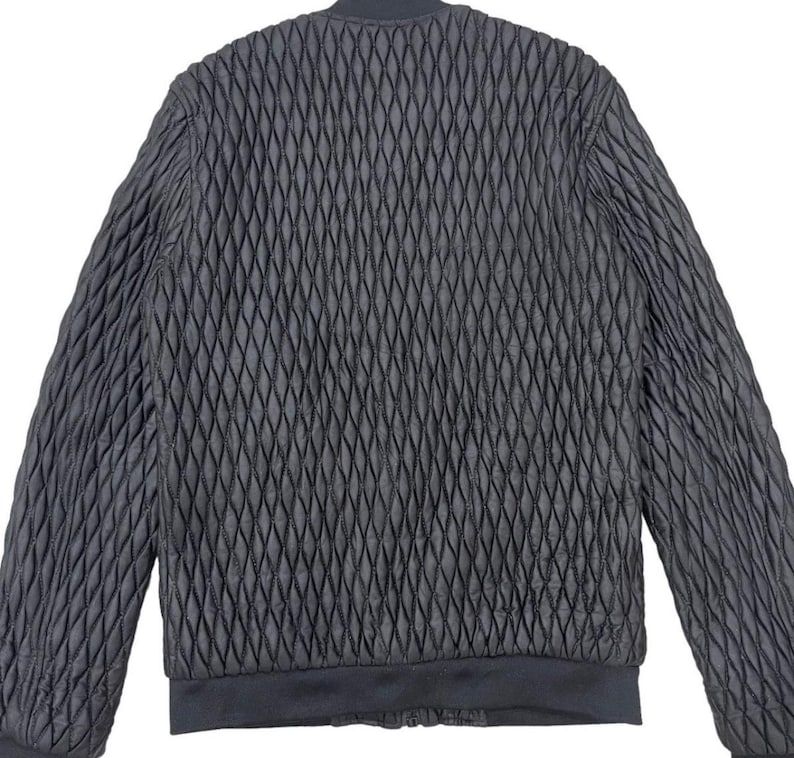 Puede incluir: Chaqueta bomber acolchada negra con un patr&oacute;n de diamantes. La chaqueta tiene cuello, pu&ntilde;os y dobladillo de canal&eacute;. La chaqueta est&aacute; hecha de un material texturizado y tiene un estilo bomber cl&aacute;sico.