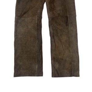 Pode incluir: Close-up de cal&ccedil;as de couro castanho. As cal&ccedil;as t&ecirc;m um design de perna reta e uma apar&ecirc;ncia texturizada e desgastada. O couro tem um acabamento fosco com varia&ccedil;&otilde;es de cor, sugerindo desgaste e envelhecimento naturais. As cal&ccedil;as s&atilde;o exibidas em um fundo branco.