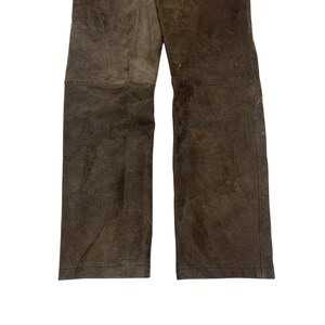 Pode incluir: Cal&ccedil;as de couro castanho com design de perna reta. As cal&ccedil;as t&ecirc;m uma apar&ecirc;ncia texturizada e uma paleta de cores neutras. A imagem mostra a parte inferior das cal&ccedil;as, destacando os detalhes do material e das costuras. Adequado para v&aacute;rias ocasi&otilde;es.