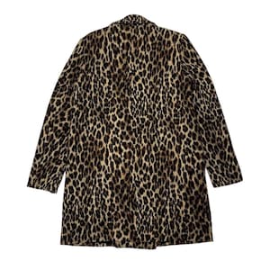 May include: A long coat with a leopard print pattern. The coat features a classic collar and long sleeves. The print is a mix of brown, tan, and black spots, creating a bold and stylish look. The coat is made of a soft, possibly woven material.