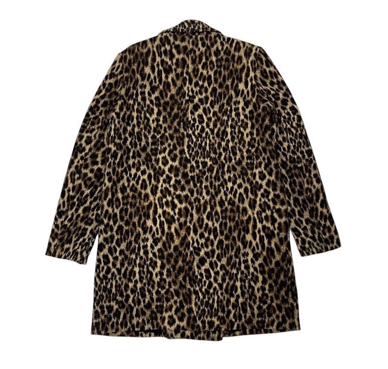 May include: A long coat with a leopard print pattern. The coat features a classic collar and long sleeves. The print is a mix of brown, tan, and black spots, creating a bold and stylish look. The coat is made of a soft, possibly woven material.