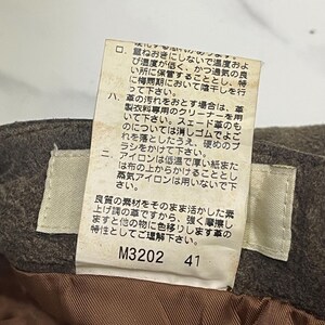 Pode incluir: Close-up de um tecido castanho com uma etiqueta branca anexada. A etiqueta tem texto japon&ecirc;s e os n&uacute;meros "M3202" e "41" impressos. O tecido parece fazer parte de uma pe&ccedil;a de vestu&aacute;rio.