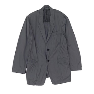 Puede incluir: Un blazer gris con cierre de dos botones, solapas con muescas y dos bolsillos delanteros. La chaqueta tiene mangas largas y un diseño clásico a medida. La tela parece ligera y adecuada para combinar.