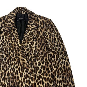 May include: A leopard print blazer with a black lining. The jacket features a classic notched collar and a double-breasted design. The print is a mix of tan, brown, and black spots. The label reads "ZARA BASIC".