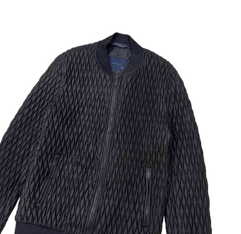 Puede incluir: Chaqueta bomber acolchada negra con un patr&oacute;n de diamantes. La chaqueta tiene una cremallera frontal, dos bolsillos laterales y un cuello y pu&ntilde;os de canal&eacute;. La chaqueta est&aacute; hecha de un material texturizado y tiene un dise&ntilde;o minimalista.