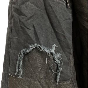 May include: Close-up of a black jacket interior with a torn pocket. The pocket is quilted with a diamond pattern. A zipper is visible at the top. The jacket appears to be made of a durable fabric.