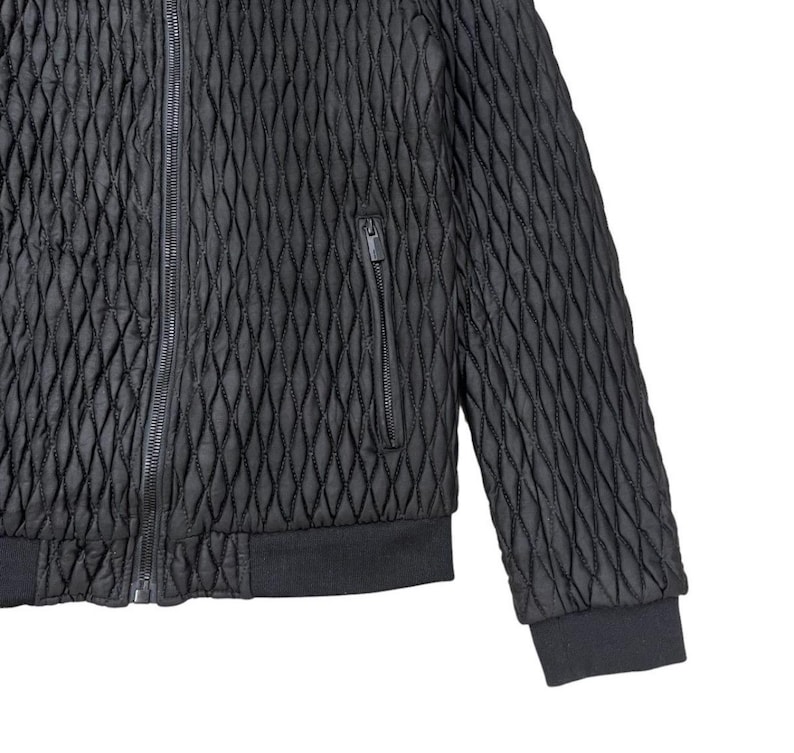 Puede incluir: Chaqueta bomber acolchada negra con un patr&oacute;n de diamantes. La chaqueta tiene cierre de cremallera completo, un bolsillo en el pecho con cremallera y pu&ntilde;os y dobladillo de canal&eacute;. La chaqueta es de material texturizado.