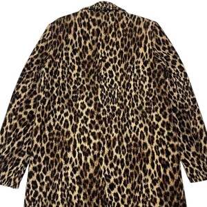 May include: A long coat with a leopard print pattern. The coat features a classic collar and long sleeves. The print is a mix of black and brown spots on a tan background, creating a bold and stylish look.