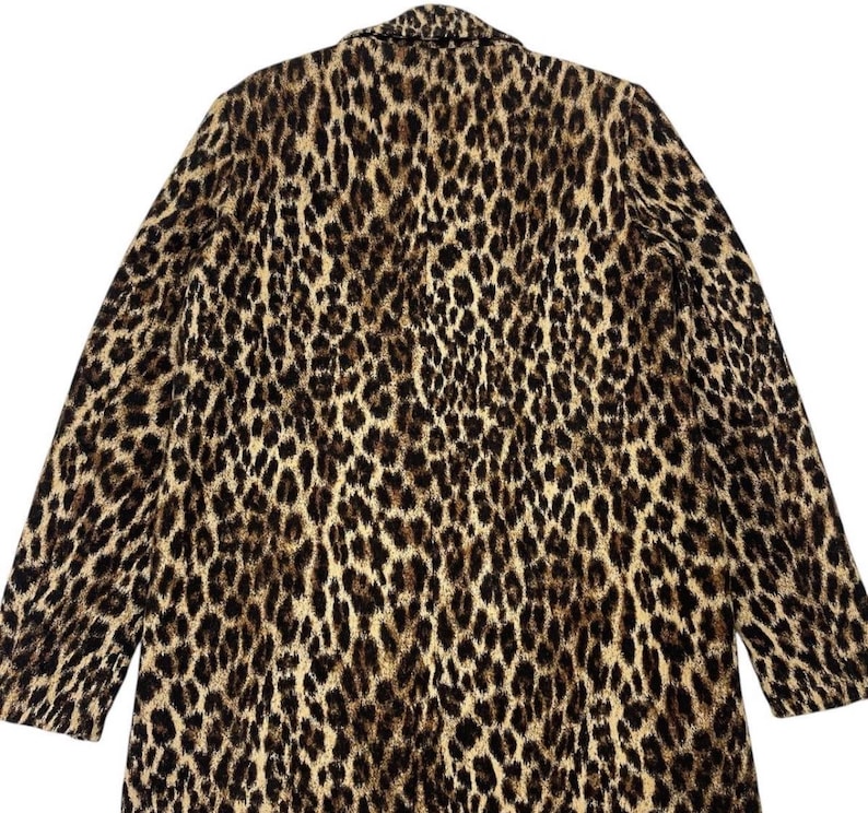 May include: A long coat with a leopard print pattern. The coat features a classic collar and long sleeves. The print is a mix of black and brown spots on a tan background, creating a bold and stylish look.