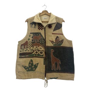 May include: A beige sleeveless vest with a full-length brown zip and a drawstring hem. The garment features a variety of dark brown, green, and black graphic prints, including a giraffe, various animal silhouettes, stars, and geometric patterns.
