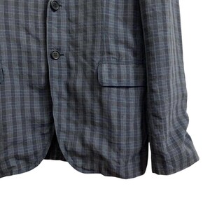 May include: A dark gray blazer with a subtle plaid pattern. The jacket features two front pockets, a chest pocket, and three buttons. The fabric appears to be a lightweight material, suitable for warmer weather.