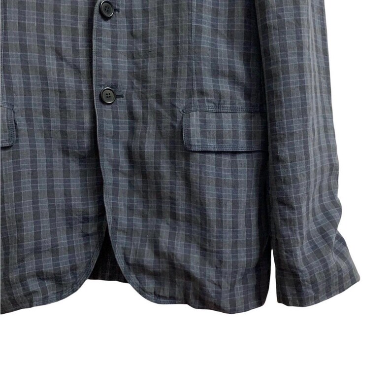 May include: A dark gray blazer with a subtle plaid pattern. The jacket features two front pockets, a chest pocket, and three buttons. The fabric appears to be a lightweight material, suitable for warmer weather.