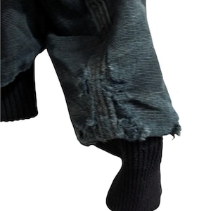 May include: Close-up of a dark blue jacket sleeve with distressed detailing at the cuff. The sleeve has a ribbed black cuff. The jacket appears to be made of a durable fabric.