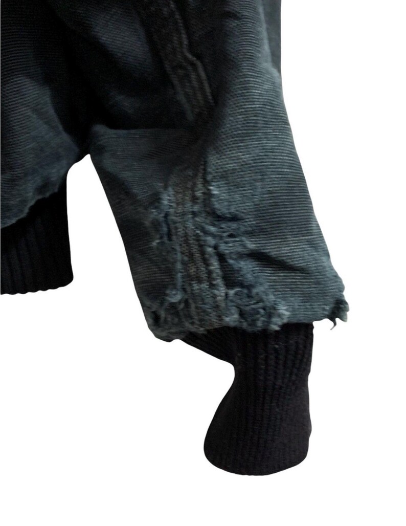 May include: Close-up of a dark blue jacket sleeve with distressed detailing at the cuff. The sleeve has a ribbed black cuff. The jacket appears to be made of a durable fabric.