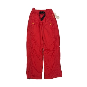 Puede incluir: Pantalones de color rojo brillante con cintura elástica, cinturón de nailon negro integrado y hebilla. Los pantalones incluyen dos bolsillos laterales con tiradores de cremallera amarillos y un pequeño logotipo amarillo bordado en el lado derecho.