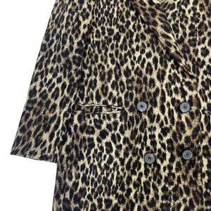 May include: A double-breasted leopard print coat with four dark buttons. The coat features a classic notched lapel and two front pockets. The animal print pattern is in shades of brown and black.