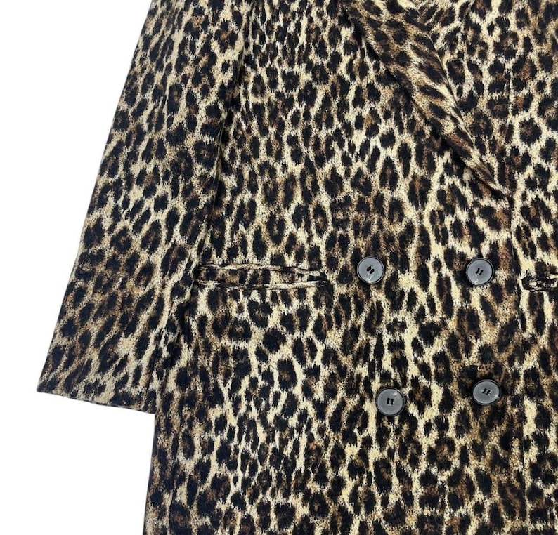 May include: A double-breasted leopard print coat with four dark buttons. The coat features a classic notched lapel and two front pockets. The animal print pattern is in shades of brown and black.