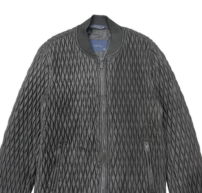 Puede incluir: Chaqueta bomber acolchada negra con un patr&oacute;n de diamantes. La chaqueta tiene una cremallera frontal, un cuello acanalado y dos bolsillos laterales. La etiqueta dice "ZARA MAN".