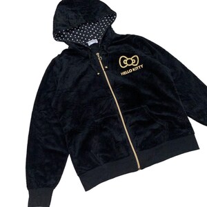 Puede incluir: Sudadera negra con cremallera dorada y logotipo de Hello Kitty. La capucha tiene un forro de lunares blancos. La chaqueta tiene un bolsillo delantero y pu&ntilde;os y dobladillo de canal&eacute;. Una prenda informal y c&oacute;moda.
