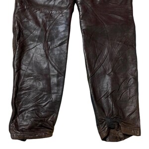 May include: Dark brown leather pants with visible stitching and a textured appearance. The pants have a classic design, with a slightly worn look. The leather appears to be soft and flexible, suggesting comfort and durability.