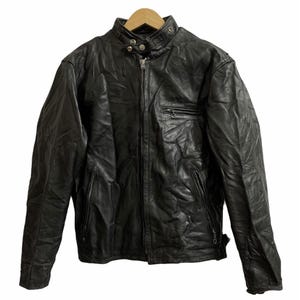 May include: A black leather jacket with a stand-up collar, a zipper closure, and a small pocket on the chest. The jacket has a classic biker style with a slightly worn appearance, suggesting it's been well-loved.