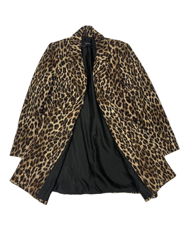 May include: A leopard print coat with a black interior lining. The coat has a classic lapel collar and a button closure. The animal print features brown and black spots on a tan background. The coat is open, displaying the black lining.