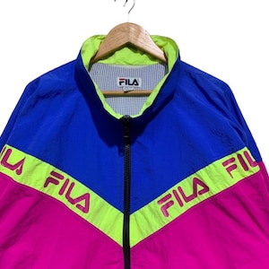 May include: A vintage Fila track jacket in blue, pink, and neon green. The jacket features a full zipper, a stand-up collar, and the Fila logo. The color-blocked design includes the Fila logo across the chest and sleeves.