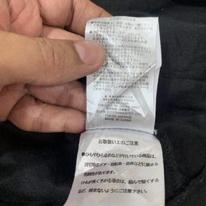 Puede incluir: Primer plano de una etiqueta de prenda negra con texto en japon&eacute;s e ingl&eacute;s. La etiqueta incluye instrucciones de cuidado y el texto "FOR SALE IN JAPAN ONLY". La etiqueta est&aacute; adherida a una tela negra.
