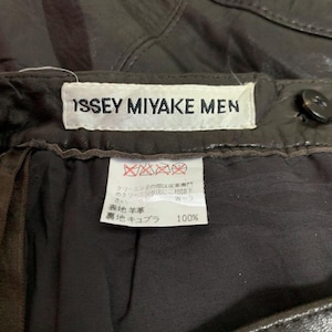 May include: Close-up of dark brown leather pants with the label "ISSEY MIYAKE MEN" visible. The label also includes Japanese text and care instructions. The pants appear to be vintage or pre-owned.