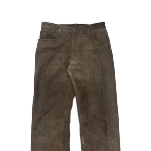 Pode incluir: Cal&ccedil;as de camur&ccedil;a castanhas com fecho de bot&atilde;o e z&iacute;per. As cal&ccedil;as t&ecirc;m dois bolsos frontais e dois bolsos traseiros. A cor neutra e o estilo cl&aacute;ssico d&atilde;o-lhe um visual casual.